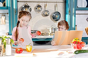 children with cookbook and vegetables cooking together