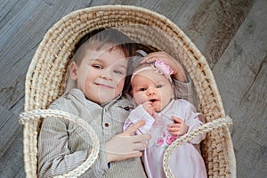 Children, cute little boy 5 years old, with him newborn sister lies in a wicker cradle