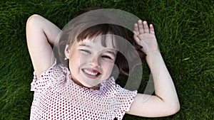 Children day. Happy cute smiling little girl lying on green grass on summer warm day. Adorable child is dreaming looking
