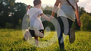 children and dog run. a boy and a girl holding hands run through the grass in the summer at sunset in the park. happy