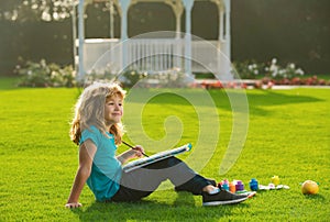 Children draw paint pictures outside, childrens creativity. Child boy draws in park laying in grass having fun on nature