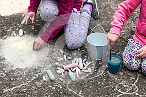 Children drawing with chalk on the concrete sitting on the ground. Art therapy, CBT, simple creativity excercises. Two girls