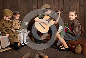 Children are dressed in retro military uniforms sitting and playing guitar, sending a soldier to the army, dark wood background, r
