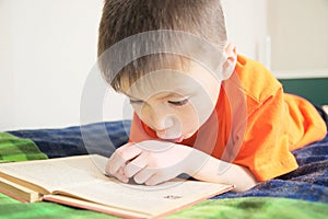 Children education, boy reading book lying on bed, child portrait with book, interesting storybook