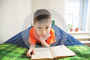 Children education, boy reading book lying on bed, child portrait smiling with book, educational interesting storybook