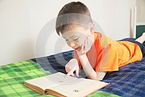 Children education, boy reading book lying on bed, child portrait smiling with book, interesting storybook