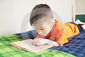 Children education, boy reading book lying on bed, child reading book with interest, educational interesting storybook