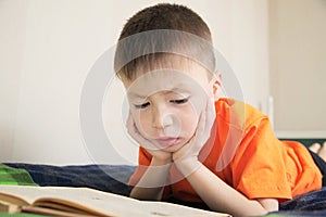 Children education, child reading book lying on bed, boy portrait with book, interesting storybook