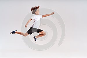 Children engaged in sport. Full-length shot of a teenage boy jumping  over grey background, studio shot