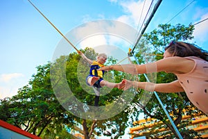 Children entertainment theme. Kid jumping on trampoline with safety rope.