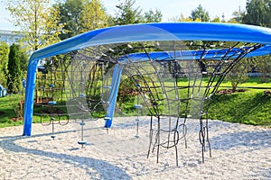 Children equipment for rope climbing with blue metal frame on modern playground in city park on sunny day