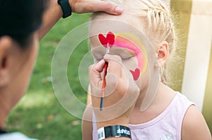 Children face painting. The artist draws a heart on the face of a child.