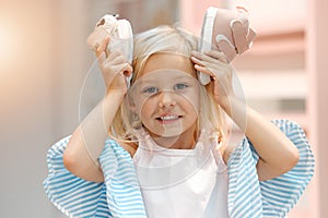 Children, fashion and clothes with shoes in girl hands against her head while shopping in a retail store. Kids, cute and