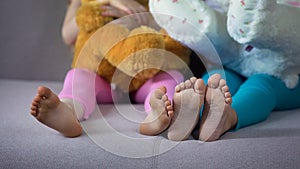 Children feet closeup, multiracial friends sitting on sofa, playing with teddies