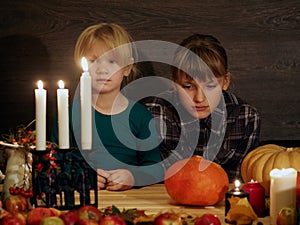 Children at the festive table, fascinated looking at the candles. Halloween.