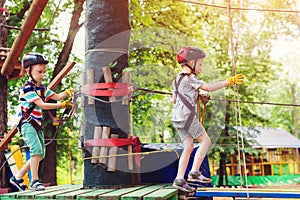 Children in forest adventure park. Kids in safety helmets, extreme sport. Summer camp. Boys enjoy climbing in the ropes course