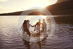 Children With Friends Enjoying Evening Swim In Countryside Lake