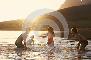 Children With Friends Enjoying Evening Swim In Countryside Lake
