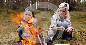 children frying sausages on skewers over a bonfire in forest. camping with kids