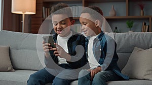 Children gadget addiction two happy laughing African American little boys brothers browsing mobile phone watching