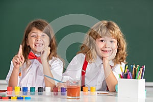 Children girl and boy drawing with coloring pens. Cute school kids painting in class at school, looking at camera