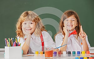 Children girl and boy drawing with coloring pens. Cute school kids painting in class at school, looking at camera