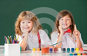 Children girl and boy drawing with coloring pens. Cute school kids painting in class at school, looking at camera