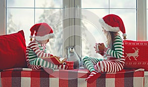 Children girl and boy in pajamas is sad on Christmas morning by window photo