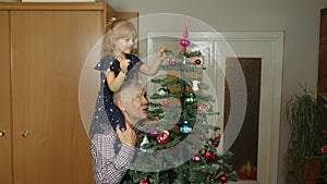 Children girl with elderly grandparent decorating artificial Christmas pine tree at old-fashion home