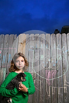 Children girl holding puppy dog on backyard wood fence