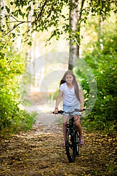 Children girl riding bicycle outdoor in forest smiling.