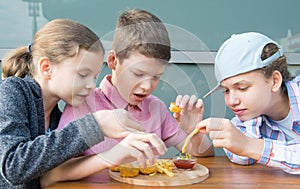 Children, girls and a boy, sit at the table and eat fast food, nuggets with sauce and French fries