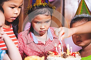 Children girls and boys lighting candle on birthday cake together in birthday party