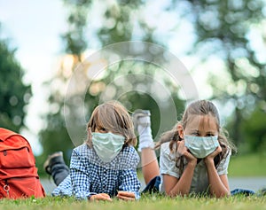 Children go back to school. Cute pupils with backpacks. Boy and girl in safety masks lie on the grass