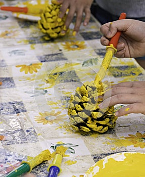 Children hands decorating pine cones with yellow paint in a creative arts and crafts workshop