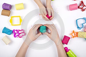 Children hands playing with colorful modeling clay on white background