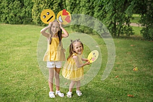 Children have fun in nature in park, holding paper emojis with different emotions on face