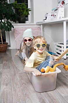 Children have fun and ride in a white plastic box. The room is a mess.