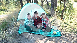 Children have video chat on laptop in the forest. Boys and girls are resting in a tent camp