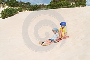 Children having fun while sliding down sand dune on sandboard