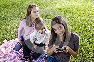 Children having picnic in park playing with smartp