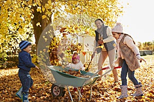 Children Helping Father To Collect Autumn Leaves In Garden