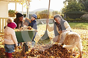 Children Helping Parents To Collect Autumn Leaves In Garden