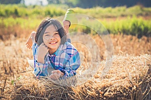 Children helping sweep haystack to pile in rice field of organic farm