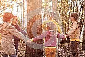 Children holding hands around a tree.