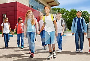 Children holding hands carry rucksacks and walk