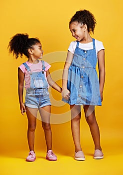 Children, holding hands and happy sisters in studio with love, care and support of family on yellow background. Cute