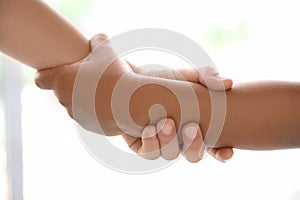 Children holding hands on light background, closeup.