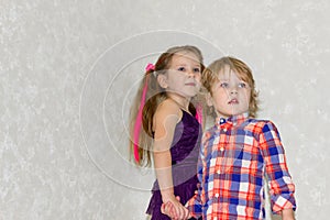 Children holding hands together stand on a light background and look into the distance