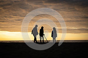 Children on holiday vacation silhouetted as they are treasure detecting at sunset on beach near ocean with metal detector sun